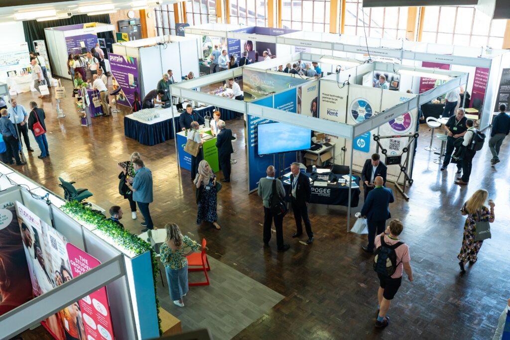 A busy exhibition hall with multiple stands and delegates walking around.